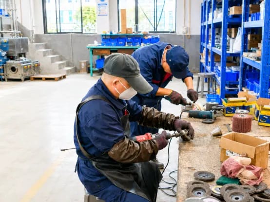 Technicians polishing metal components with handheld tools at a workshop bench