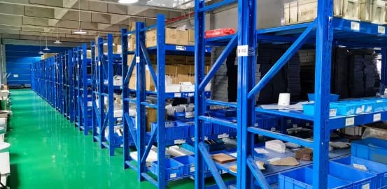 Blue shelving with labeled storage locations, boxes and machine components